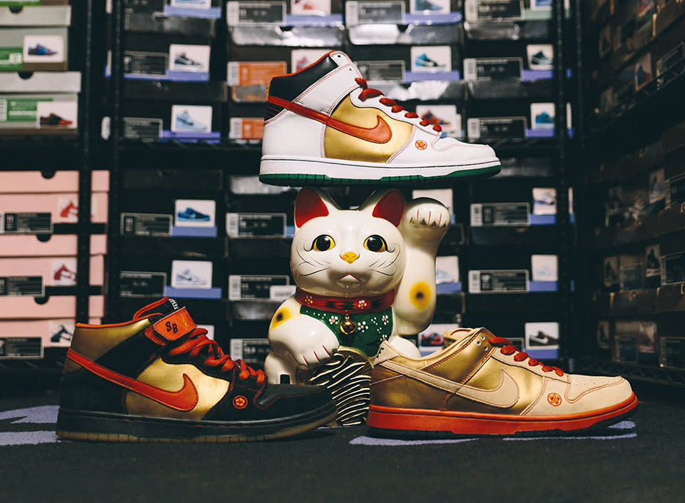 A store display shows three pairs of sneakers — in various color combinations of gold, red, black and white — against a background of shelves with dozens of boxes of shoes stacked up.