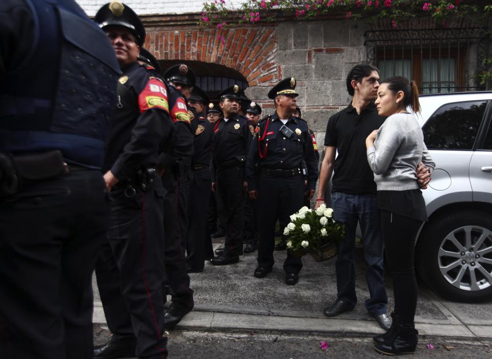 A couple holding flowers stand behind police officers outside the home of Colombian Nobel Prize laureate Gabriel Garcia Marquez in Mexico City