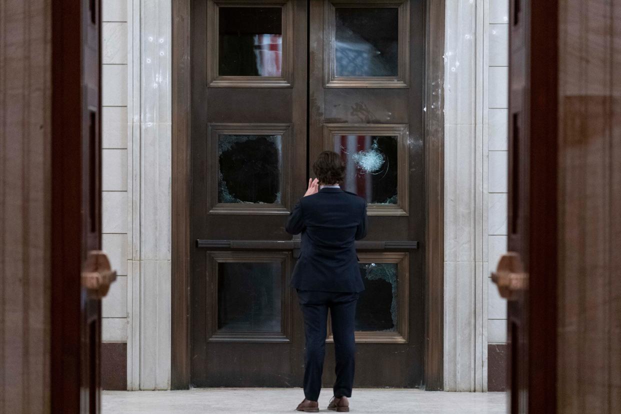 A man takes a photo of broken windows near the Rotunda in the early morning hours of Thursday, Jan. 7, 2021, after protesters stormed the Capitol in Washington on Wednesday.