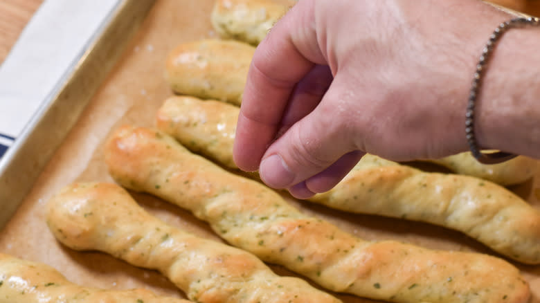 hand sprinkling breadsticks with salt