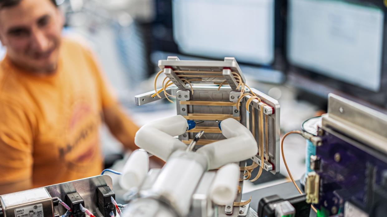  A robotic hand-like device reaching towards rubber bands in a lab. 