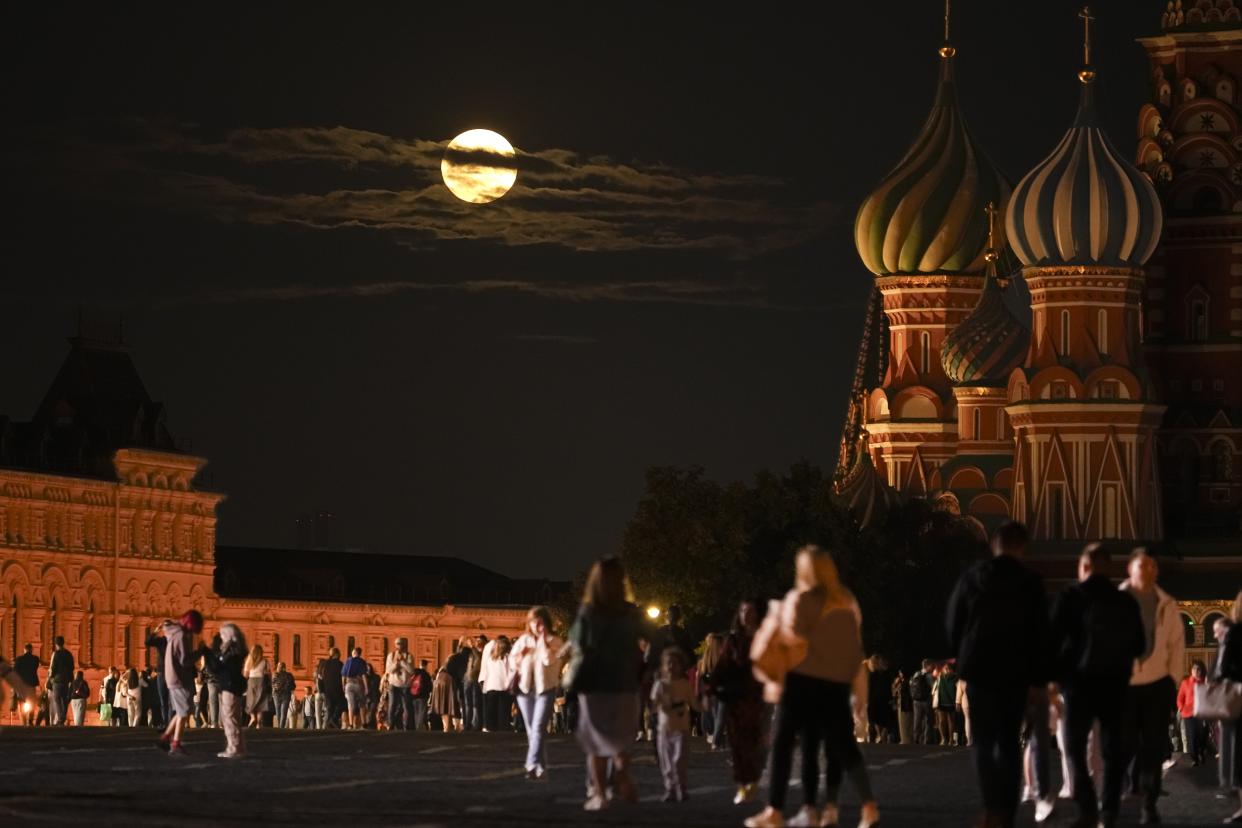 The August Super Blue Moon sets behind a historical building and the St. Basil's Cathedral, right, as people walk in Red Square in Moscow, Russia, Wednesday, Aug. 30, 2023. The cosmic curtain rises Wednesday night with the second full moon of the month, the reason it is considered blue. It is dubbed a supermoon because it is closer to Earth than usual, appearing especially big and bright. (AP Photo/Alexander Zemlianichenko)