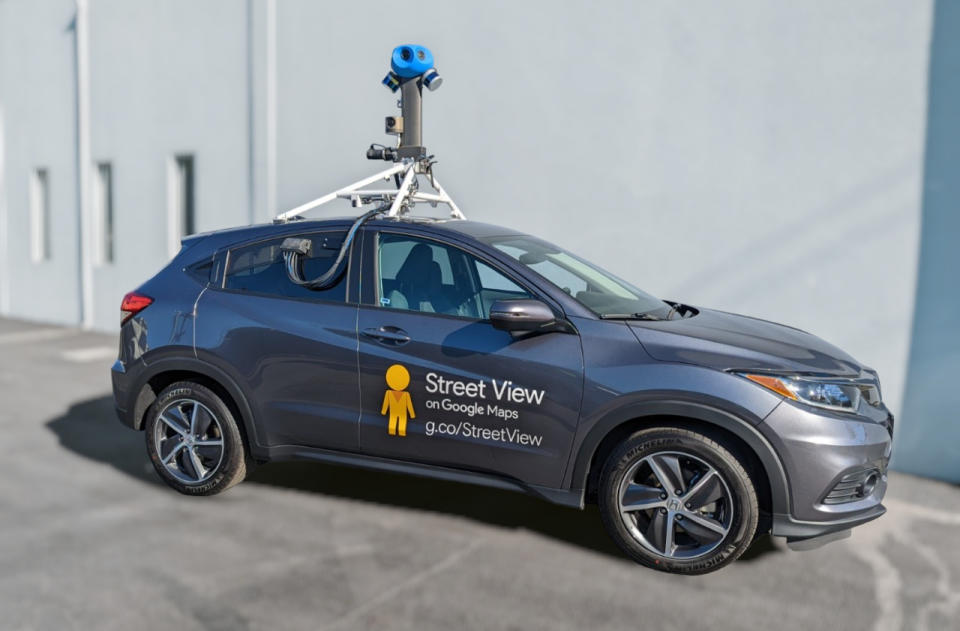 An ultra-compact SUV fitted with a Google Street View camera perched on its roof. It sits on gray pavement in front of a white wall.
