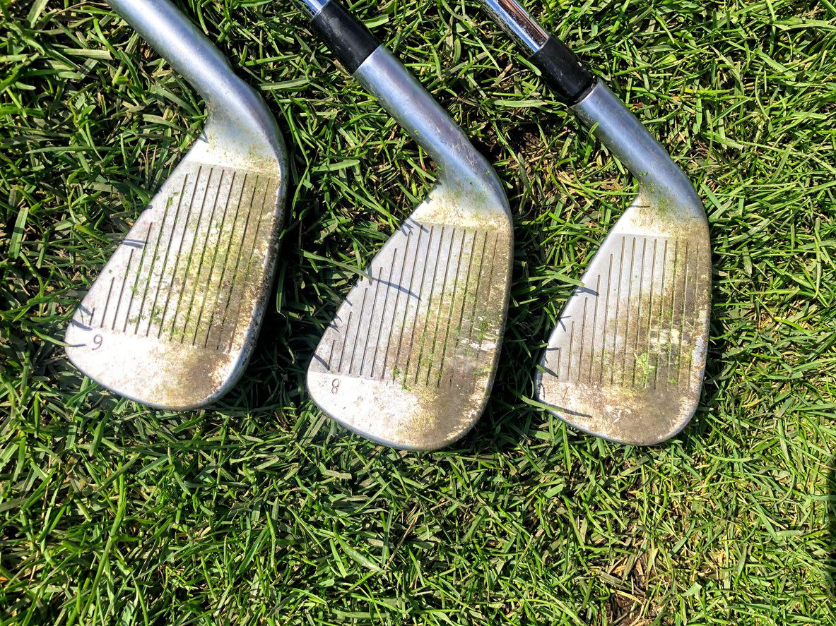 A closeup view of three golf irons with dirty grooves that need cleaning