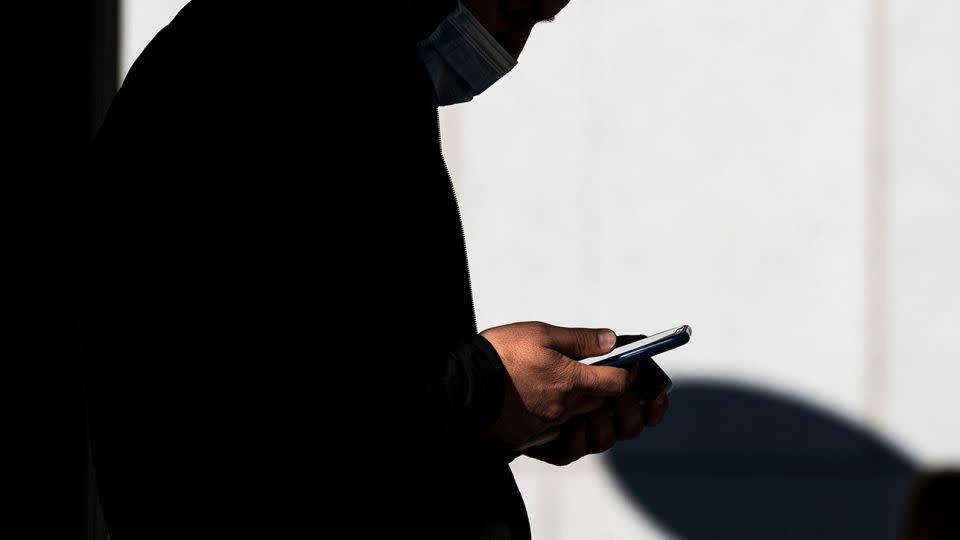 A pedestrian uses a smartphone in front of a store in Walnut Creek, California, in January 2022. - David Paul Morris/Bloomberg/Getty Images