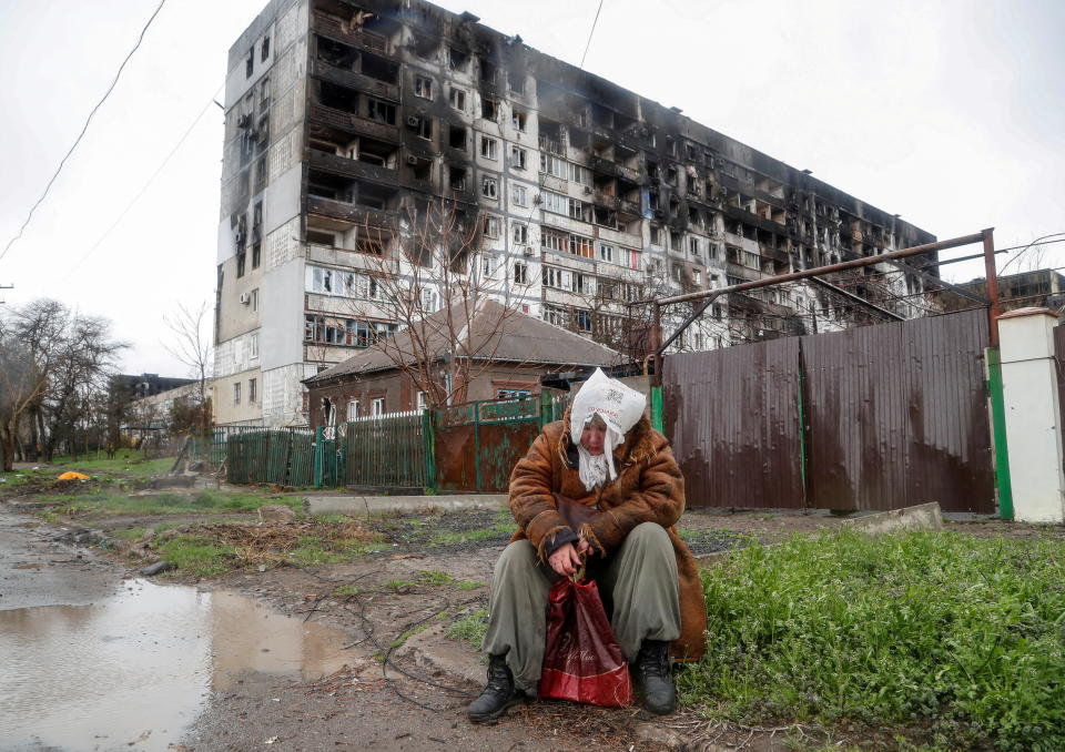 A woman sits in front of a residential building damaged in the course of Ukraine-Russia conflict, on a rainy day in the southern port city of Mariupol, Ukraine April 13, 2022.  REUTERS/Alexander Ermochenko      TPX IMAGES OF THE DAY