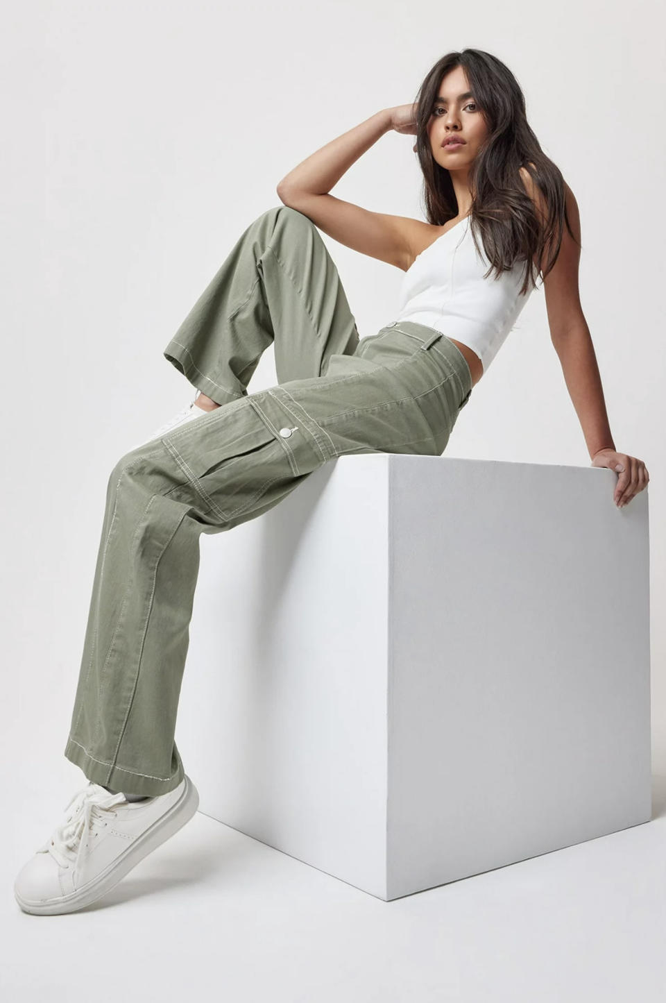 model wearing green denim cargo pants with white sneakers and a white tank top