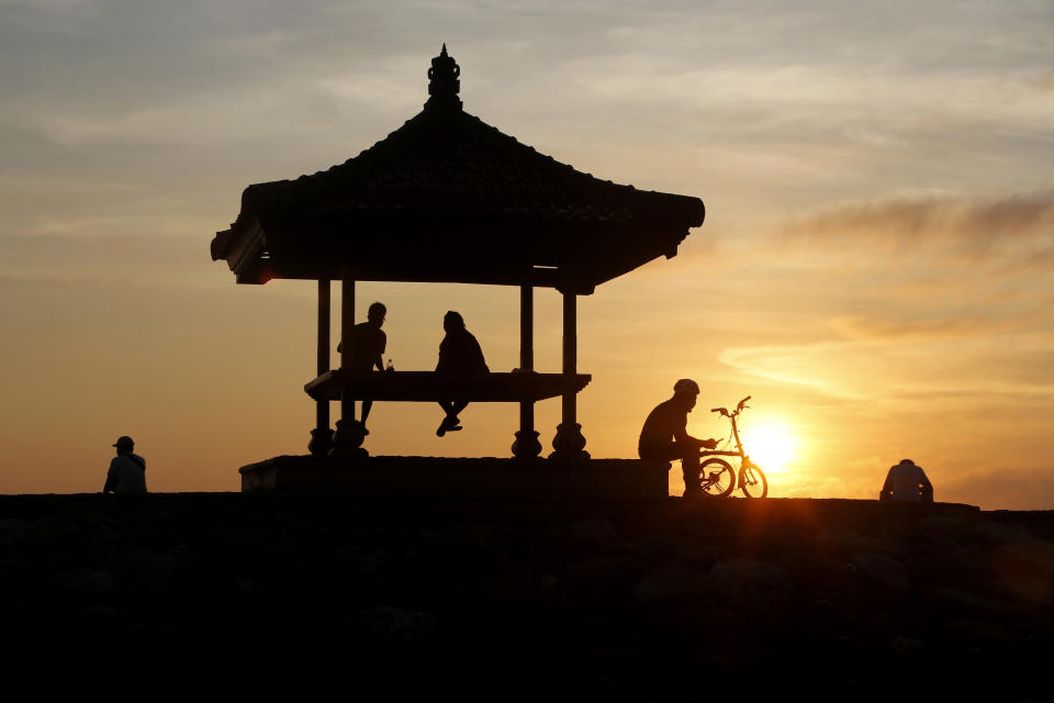 People watch the sun rise at the Sanur Beach in Denpasar, Bali, Indonesia, Thursday, Oct. 28, 2021. Indonesians are looking ahead warily toward the upcoming holiday travel season, anxious for critical tourist spending but at the same time worried that an influx of millions of visitors could lead to a new coronavirus wave just as the pandemic seems to be getting better. (AP Photo/Firdia Lisnawati)