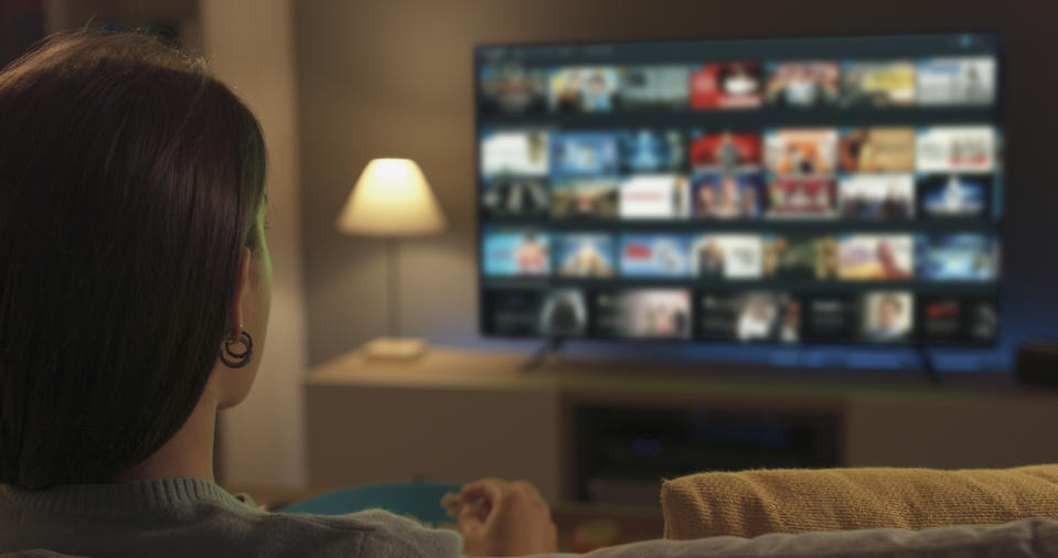 Young woman relaxing on the couch at home and watching videos on demand on her TV, entertainment concept