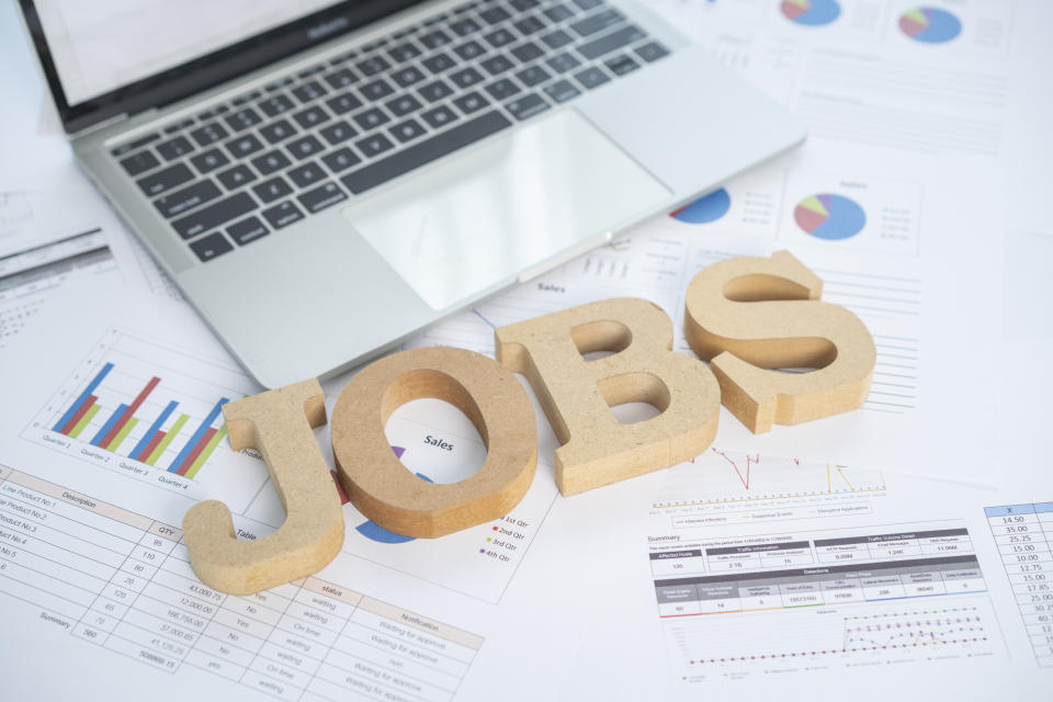 Wooden "JOBS" text on paper with charts and a laptop in the background