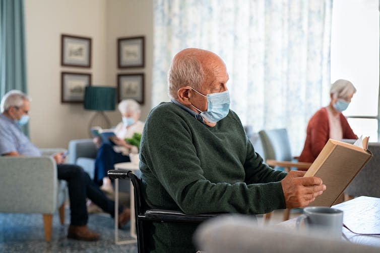 A man wearing a mask and reading a book in a care home.