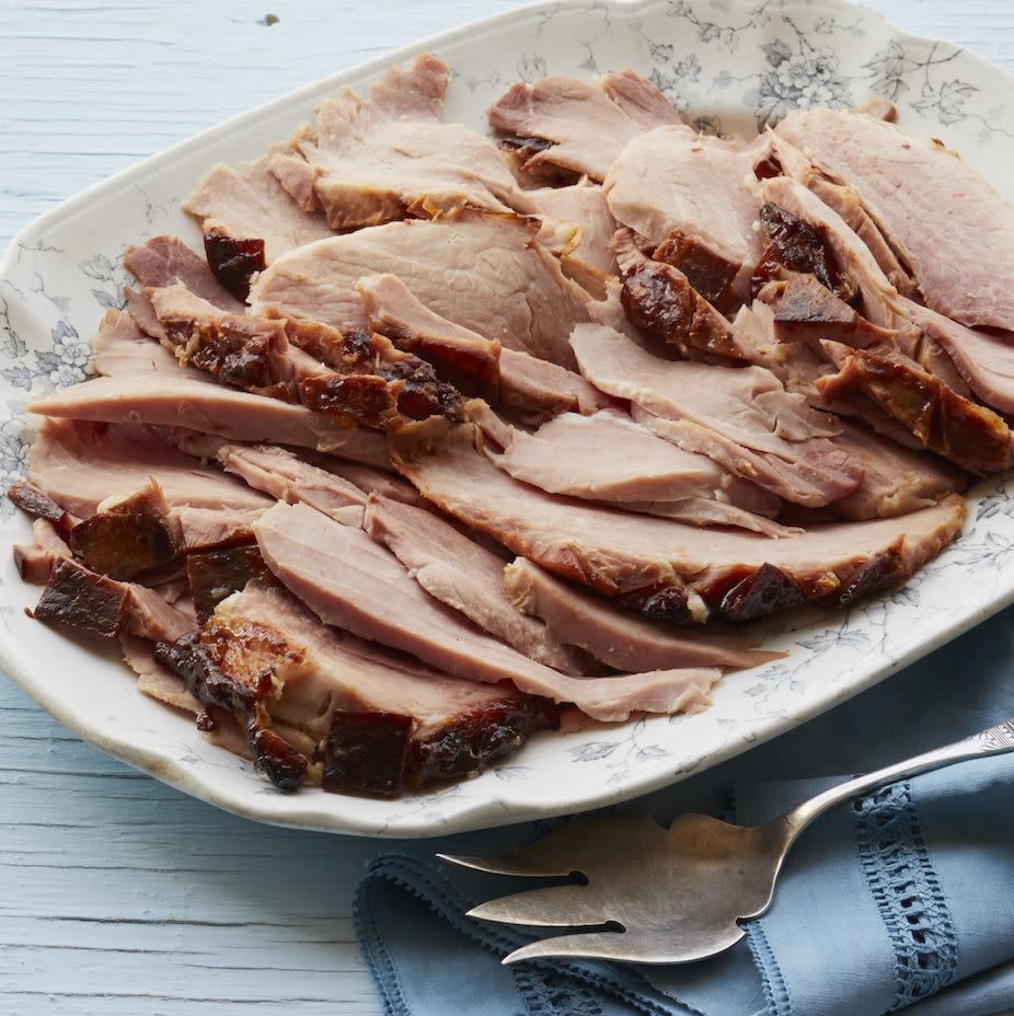 root beer glazed ham on white platter with serving fork and blue napkin