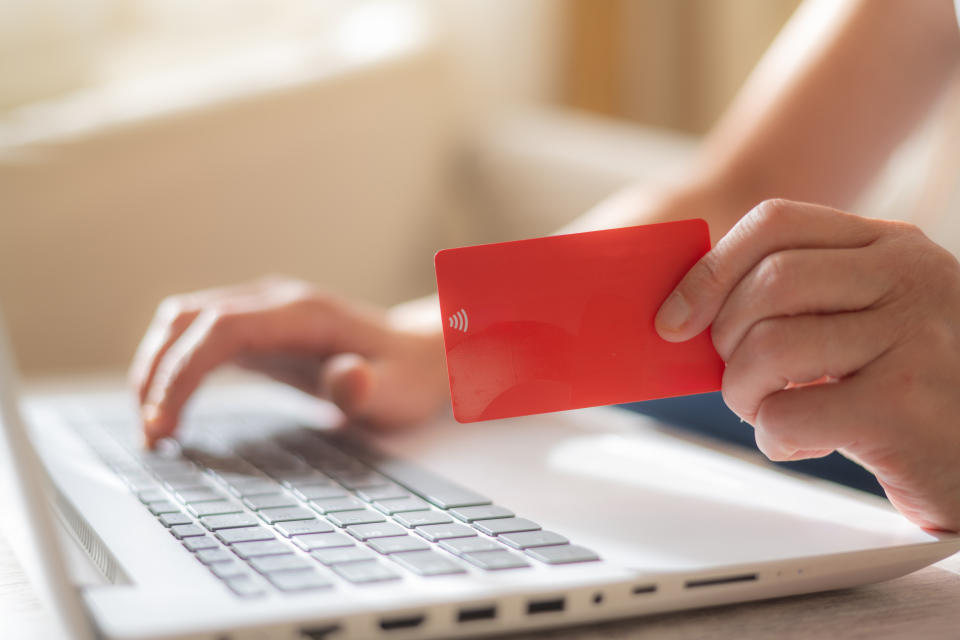 A person holds a red contactless payment card in their right hand and types on a laptop with their left hand