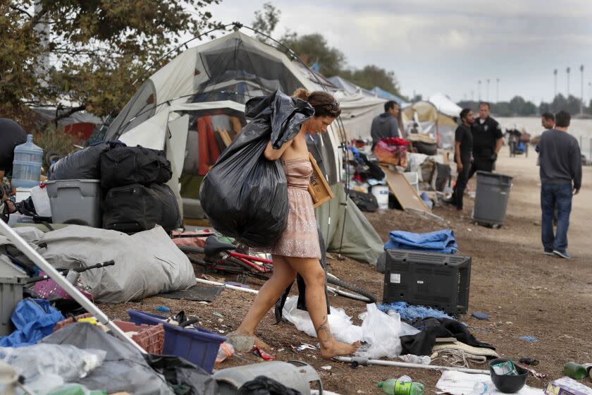 SANTA ANA, CALIF. --FRIDAY, NOV. 10, 2017: "Just because it's an ugly day doesn't mean I have to be ugly," said Morgan "Mermaid" Gallerito, shown wearing a glamorous dress while being evicted with her belongings from a large homeless encampment along the Santa Ana River trail Friday, Nov. 10, 2017. The homeless were evicted by Orange County Sheriff's, Anaheim, Orange, and Fountain Valley Police officers who swept through the encampment to enforce an eviction notice that began Friday between Warner Ave. and Edinger Ave. along the Santa Ana River trail on the border of Fountain Valley and Santa Ana. Campers were generally heading to nearby streets and further north near Katella Ave. in Anaheim where they are not arrested. The Santa Ana River trail homeless sweep Friday calls for permanently closing the west side of the flood control channel between 17th Street in Santa Ana and Adams Avenue in Huntington Beach, a move that is expected to displace a large population of homeless people who have set up camp along the river. Neighbors and people living in the camps estimate the number at at least 150. The question of where they will move remains unanswered. Homeless people and their advocates say the county is simply pushing the issue down the road instead of solving it. Armories might provide temporary shelter for those displaced from the river trail. The National Guard armory in Santa Ana is open as a nightly sleeping area for the homeless during the winter. The Fullerton armory is expected to begin operating as a nighttime shelter Nov. 16. Some homeless people say they are resistant to shelters because they would have to get rid of their pets and stay in cramped conditions with little or no privacy. (Allen J. Schaben / Los Angeles Times)