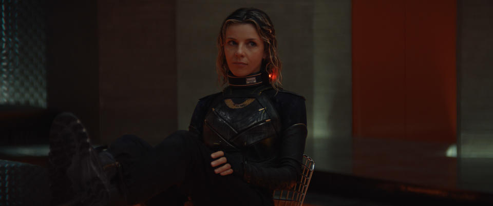 Character in a black costume with armor panels rests against an orange backdrop