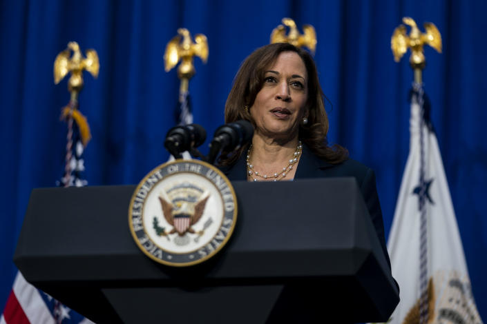 Kamala Harris stands at podium with the vice presidential seal in front of a blue curtain and flags.
