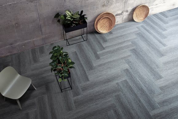 Variegated gray herringbone-style modular flooring by Interface, with two planters, a white chair, and three decorative plates on top.