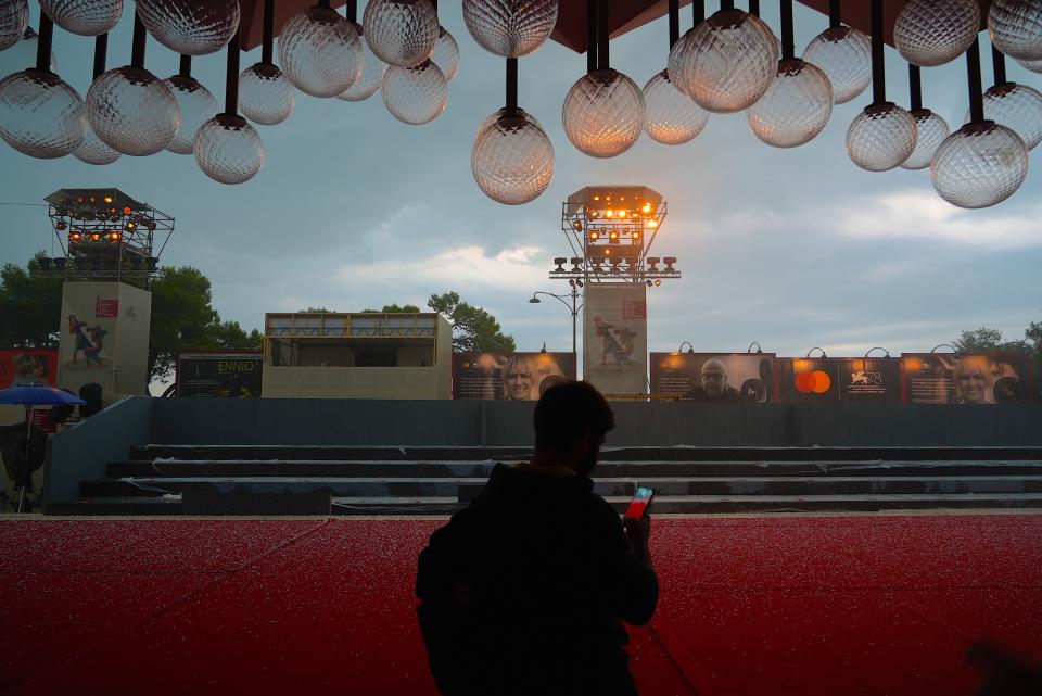 A worker uses his phone to scan hailstones on the red carpet of the 78th edition of the Venice Film Festival at the Venice Lido, Italy, Monday, Aug. 30, 2021. The festival opens Sept. 1 through Sept. 11. (AP Photo/Domenico Stinellis)