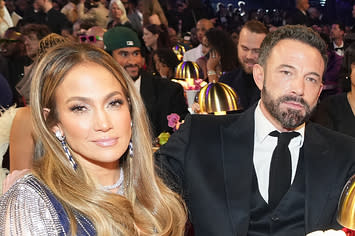 Jennifer Lopez sits with her hand wrapped around her knee and smiles as Ben Affleck appears bored sitting next to her