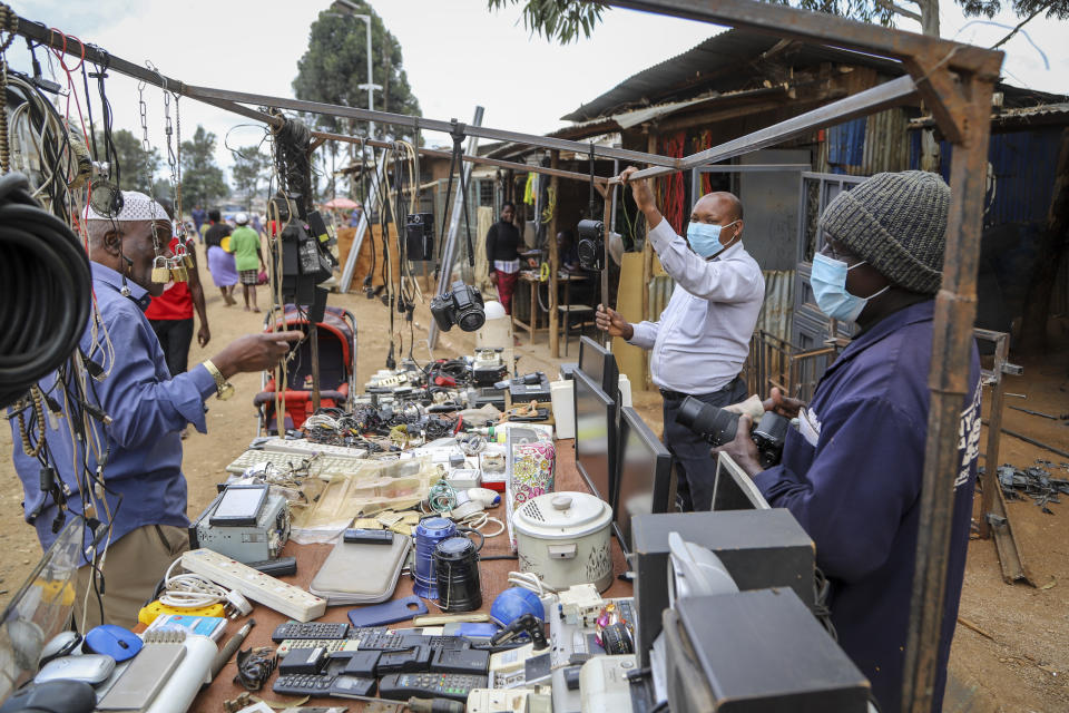 FILE - Onesmus Mauta, center, and Masumba, right, wear masks as they speak to a client, left, at their secondhand electronics street stall in the Kibera neighbourhood of Nairobi, Kenya on March 20, 2020. (AP Photo/Patrick Ngugi, File)