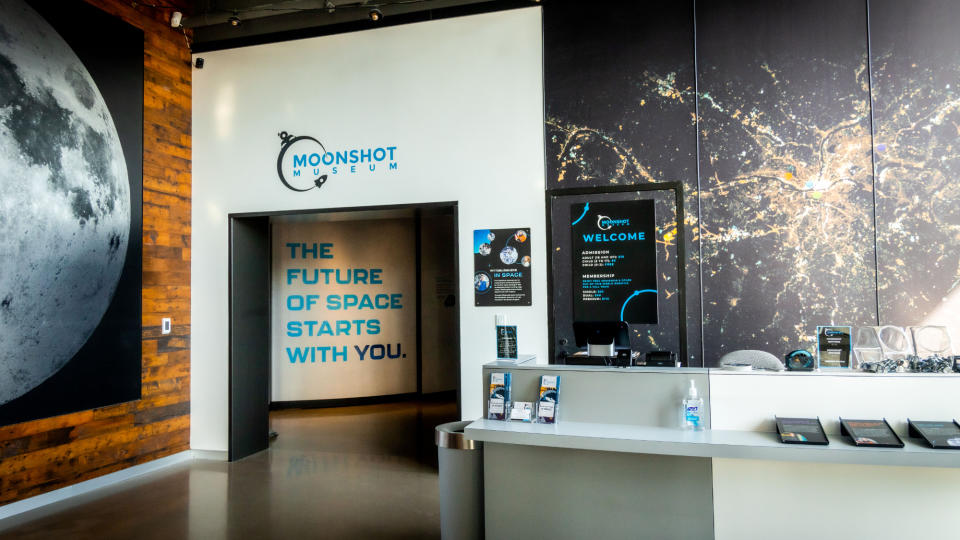 museum exhibition with a large photo of the moon on a wall, next to a doorway, with writing inside 