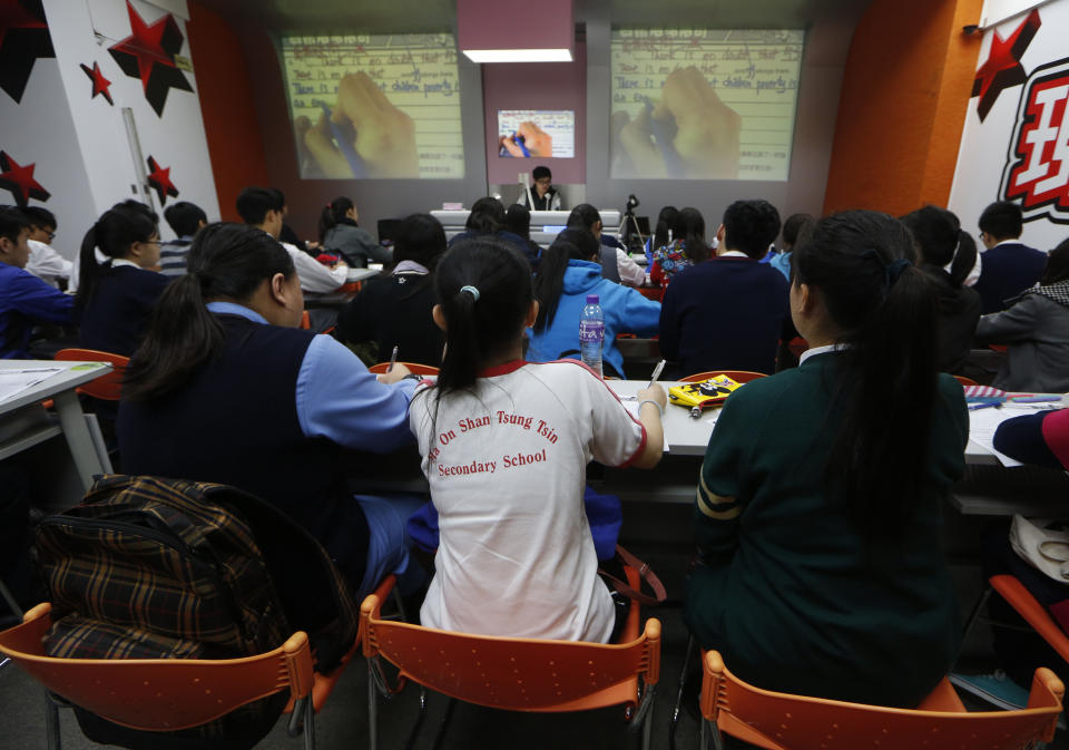 In this Dec. 9, 2013 photo, English grammar tutor Tony Chow, center in the background, gives a lesson to his students in a classroom of Modern Education in Hong Kong. The 30-year-old teaches English grammar to thousands of secondary school pupils, who attend his after-school lessons or watch video replays of them at Modern Education’s 14 branches. Chow is a celebrity tutor in Hong Kong, where there’s big money to be made offering extracurricular lessons to parents desperately seeking an edge for their children preparing for the city’s intense public entrance exam for university. (AP Photo/Kin Cheung)