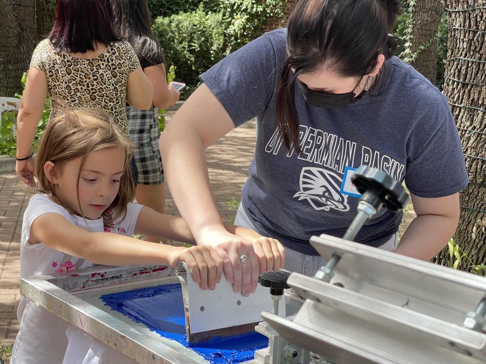 An art student from the University of Texas Permian Basin helps a child create a screen-printed T-shirt during a Pots-n-Prints event. Pots-n-Prints is a mobile studio that takes printmaking and ceramics to the rural areas in Southwest and West Texas.