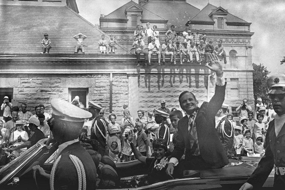 FILE - In this Sept. 6, 1969 file photo, people sit on the roof ledge of the Auglaize County Courthouse to cheer hometown hero Neil Armstrong waving to the crowd during a parade honoring him for his moon-walk feat. Also shown is his wife, Jan, and son, Eric, in the parade in Wapakoneta, Ohio. Neil Armstrong helped put Wapakoneta on the map July 20, 1969, when he became the first human to walk on the moon. The late astronaut remains larger than life in the city 60 miles (96.56 kilometers) north of Dayton, where visitors are greeted by the space base-shaped top of the space museum named for him as they exit Interstate 75. (AP Photo)