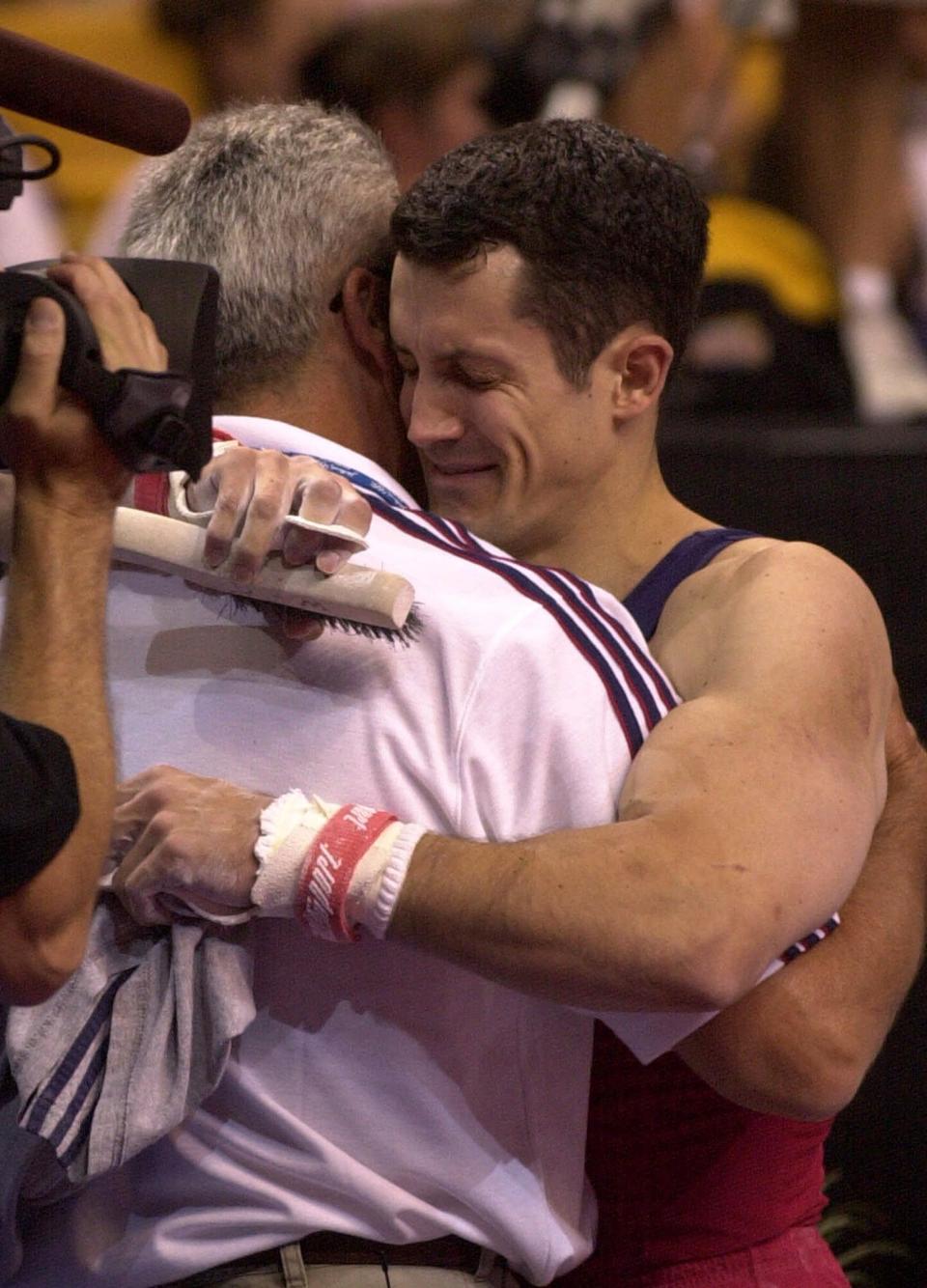 FILE - John Roethlisberger, of Falcon Heights, Minn., hugs his dad Fred after his final event in the men's 2000 U.S. Olympic Gymnastics Trials in Boston, in this Saturday, Aug. 19, 2000, file photo. Roethlisberger was chosen for the U.S. Olympic team. The cutback in NCAA athletic programs due to the COVID-19 pandemic is being felt acutely in men's gymnastics. For decades Division I programs have produced an overwhelming majority of the US Olympic team. The number of Division I programs, however, is shrinking. The University of Minnesota and the University of Iowa will stop offering it as a scholarship sport at the end of the month. That will drop the number of Division I schools to 11. (AP Photo/Elise Amendola, File)