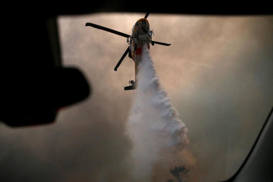 A helicopter makes a water drop as the Woolsey Fire burns in Malibu, California (REUTERS)