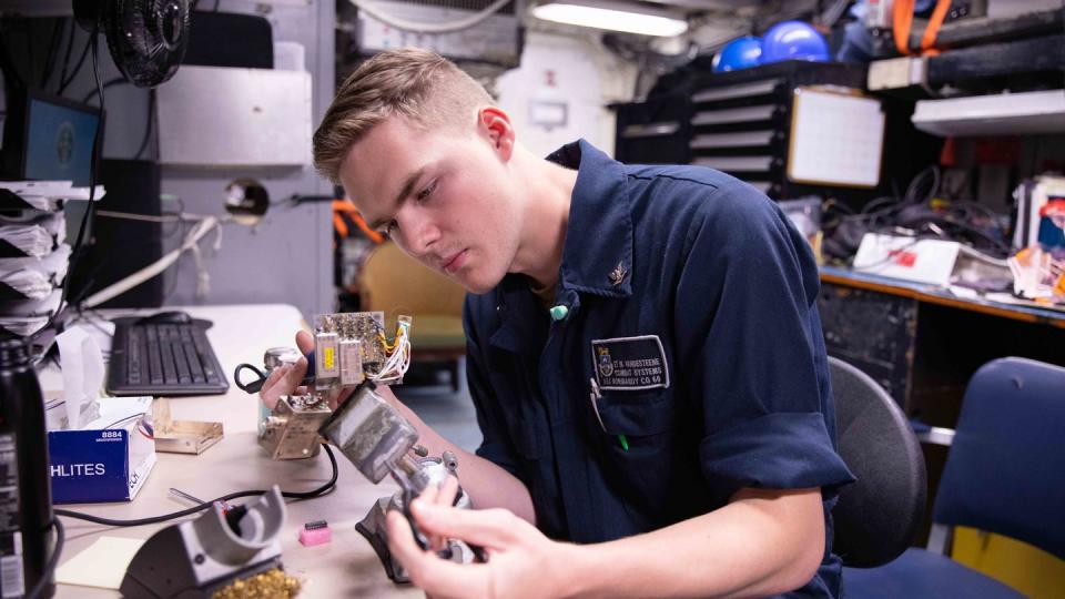 Electronics Technician 3rd Class Nicholas Vandesteene solders a microchip onto a radio’s circuit board while underway on the U.S. Navy cruiser Normandy. (MC2 Malachi Lakey/U.S. Navy)