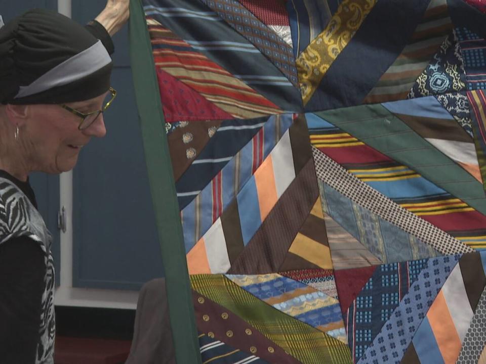 Paula Gallant holds up the quilt she made for her husband, crafted from dozens of old neckties a neighbour gave her. (Brittany Spencer/CBC - image credit)