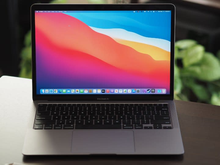 Apple M1 MacBook Air deschis pe un birou cu plante în fundal.