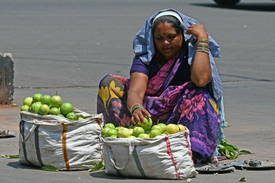 A fruit vendor covers her head with a cloth while waiting for customers by a roadside on a hot summer day in Hyderabad on April 25