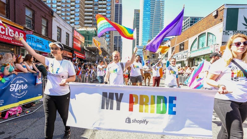 Members of a LGBT pride parade walk down a Toronto street holding a "My Pride" banner with the shopify logo.