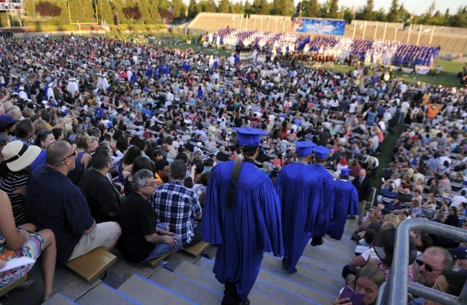 Graduating seniors including Christian Titman, wearing a feather at the end of the line, bottom center, enter Lamonica Stadium for Clovis High’s graduation ceremony.