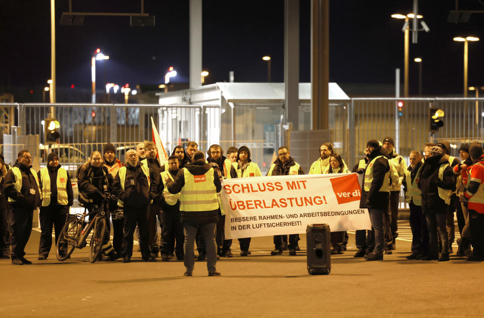 Strikers in warning clothing hold a banner of the trade union Verdi with the inscription: "End with overload!" in Cologne, Germany, Sunday, Feb. 26, 2023. Airport security staff at Cologne Bonn Airport are on strike for better wages since this evening. (Thomas Banneyer/dpa via AP)