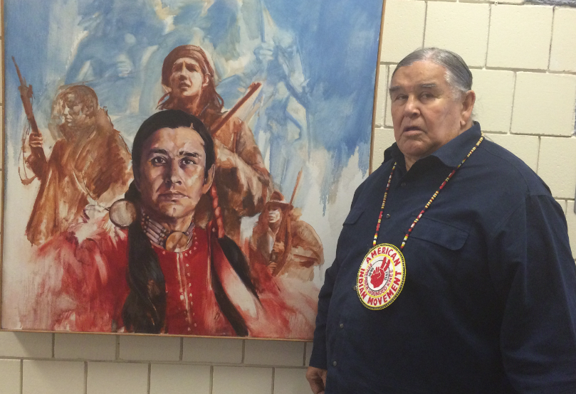<em>Clyde Bellecourt with Wounded Knee portrait at the American Indian Movement Interpretive Center in Minneapolis in August 2015. (Photo/Levi Rickert)</em>