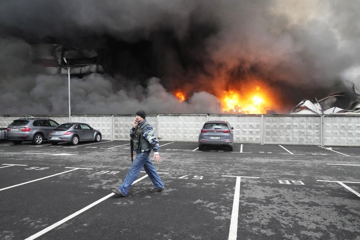A Ukrainian serviceman walks past as fire and smoke rises over a damaged logistic center after shelling in Kyiv, Ukraine, Thursday, March 3, 2022.