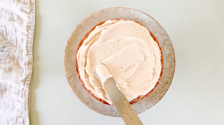 Spreading cinnamon-cashew frosting on vegan carrot cake with spatula on serving platter