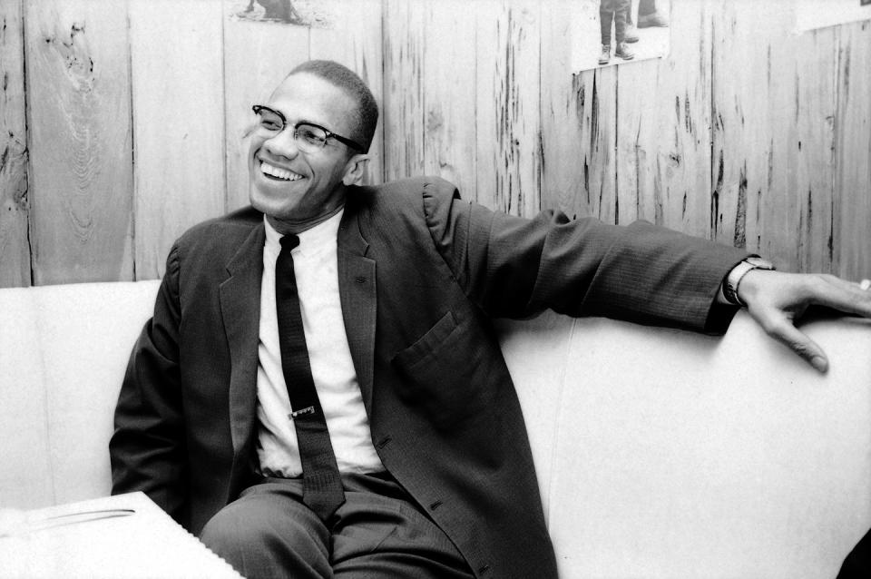 black and white photo of malcolm x sitting in a booth, smiling
