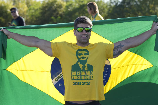 A supporter holds Brazil's national flag as he waits for the arrival of Brazil's Former President Jair Bolsonaro outside the airport in Brasilia, Brazil, Thursday, March 30, 2023. Bolsonaro arrived back in Brazil on Thursday after a three-month stay in Florida, seeking a new role on the political scene. (AP Photo/Eraldo Peres)