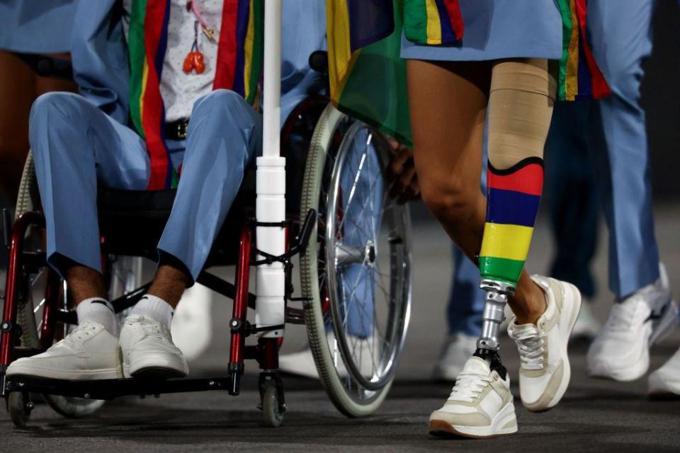 The lower bodies of two members of the Mauritius delegation are pictured in a parade at the Place de la Concorde during the Paris 2024 Paralympic Games. One person sits in a wheelchair wearing blue trousers and white trainers. The other has a prosthetic leg in the colours of Mauritius' national flag - which is yellow, green, red and blue.