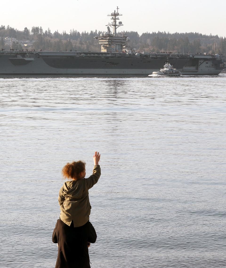 Family and friends of the sailors aboard the USS Theodore Roosevelt (CVN-71) wave from the shore of Bachmann Park in Bremerton, Wash. as the aircraft carrier departs Puget Sound Naval Shipyard after its 18-month overhaul, on Friday, March 17, 2023.