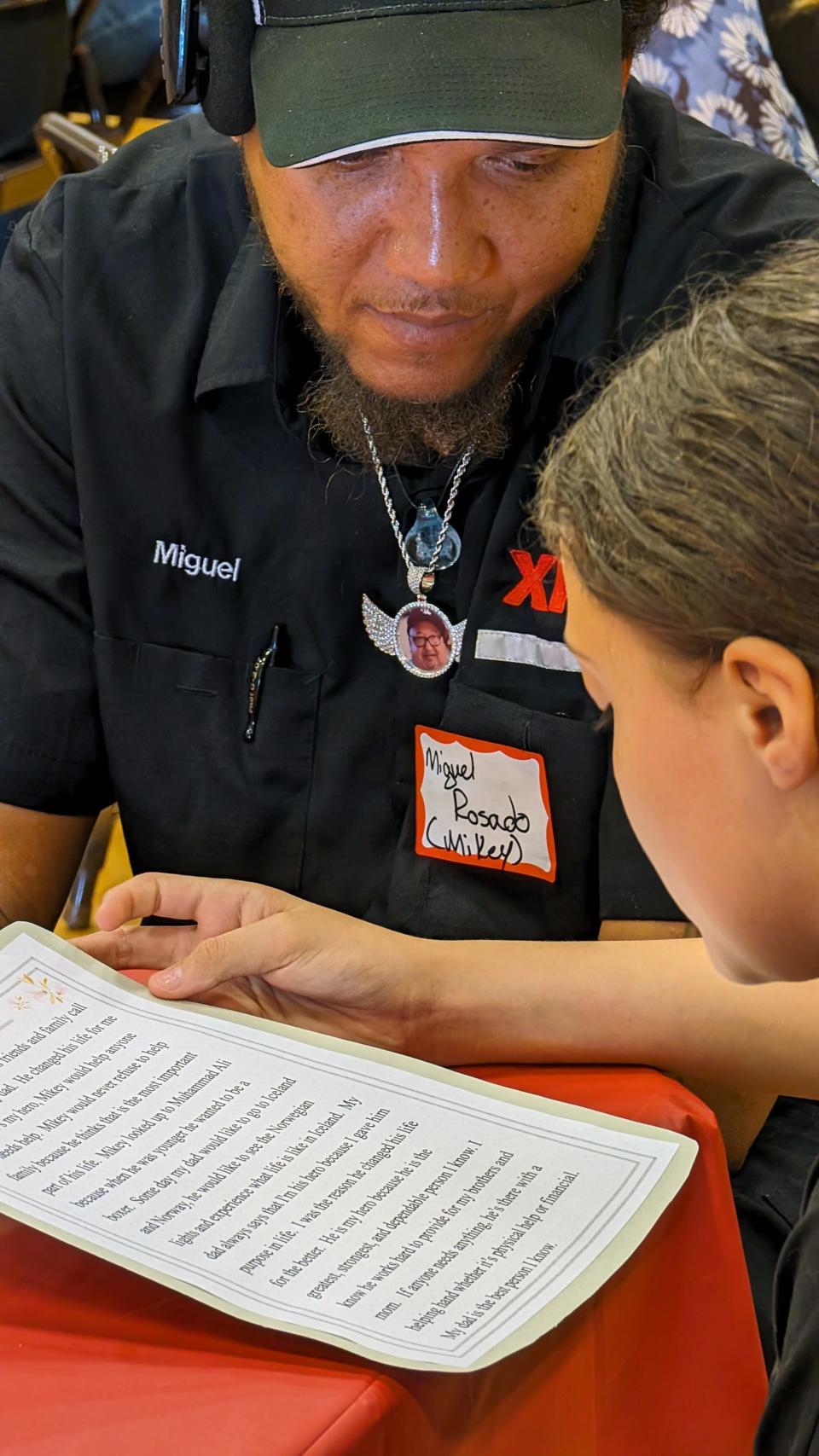 Miguel Rosado, top, listens to his daughter Mikalyn read her essay. Rosado, was unaware that he was named her hero before he arrived at the school.