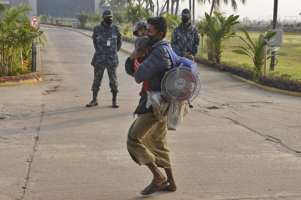 A Rohingya refugee carries a child and walks past soldiers to board a naval vessel to be relocated to the island of Bhasan Char, in Chattogram, Bangladesh, Saturday, Jan. 30, 2021. Authorities in Bangladesh sent a group of Rohingya refugees to a newly developed island in the Bay of Bengal on Saturday despite calls by human rights groups for a halt to the process. The government insists the relocation plan is meant to offer better living conditions while attempts to repatriate more than 1 million refugees to Myanmar would continue. (AP Photo/Azim Aunon)