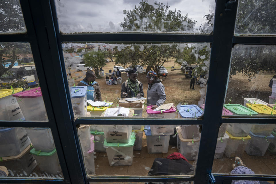 An electoral worker stands with ballot boxes lined up and ready to be stored at a collection and tallying center in Nairobi, Kenya Wednesday, Aug. 10, 2022. Kenyans are waiting for the results of a close but calm presidential election in which the turnout was lower than usual. (AP Photo/Ben Curtis)