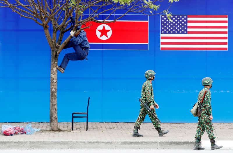 A worker is seen on a tree next to a banner showing North Korean and U.S. flags ahead of the North Korea-U.S. summit in Hanoi