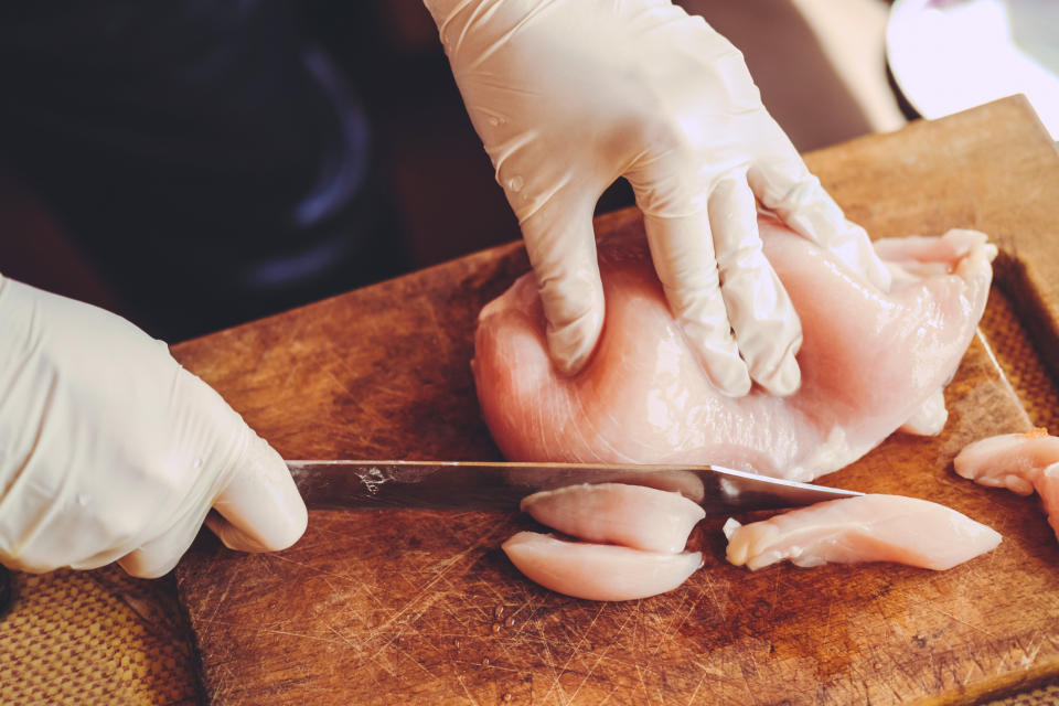 Gloved hands cut into a raw chicken breast