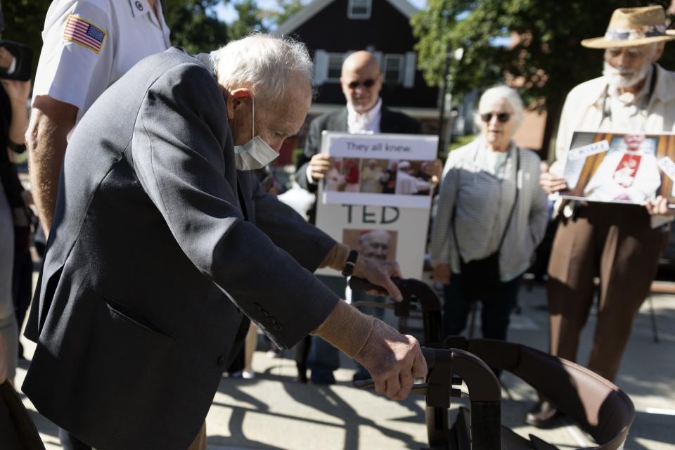 Demonstrators watch as former Cardinal Theodore McCarrick leaves Dedham District Court after his arraignment, Friday, Sept. 3, 2021, in Dedham, Mass. McCarrick has pleaded not guilty to sexually assaulting a 16-year-old boy during a wedding reception in Massachusetts nearly 50 years ago. (AP Photo/Michael Dwyer)